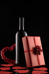 Gift box, wine bottle and red hearts on black background.