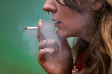 Closeup cropped shot of lower half of caucasian woman's face smoking hand rolled marijuana joint....