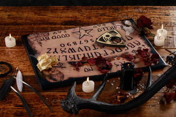 Talking board and planchette, also known as Ouija board, used for communicating with the dead and other spirits. The atmosphere of black art with candles and horns of the animal.