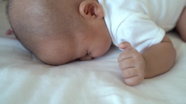 Newborn baby kid who toss and turn, sleeping on his stomach on bed at home. Asian child bottom up sleeping position