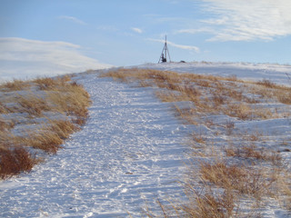 Winter landscape with a path to the hill. Flagpole on the hill. Blue sky