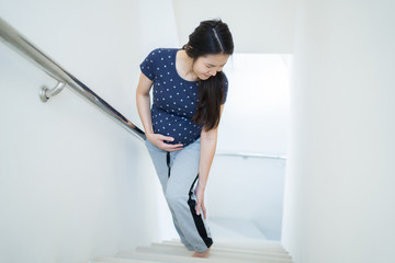 Asian woman is pregnant, she is in pain, cramps while walking up the stairs.