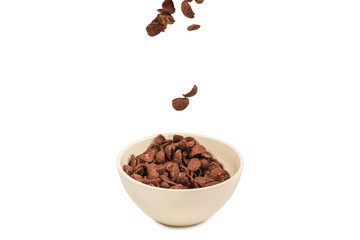Chocolate corn flakes falling to the white bowl isolated on white. Motion.