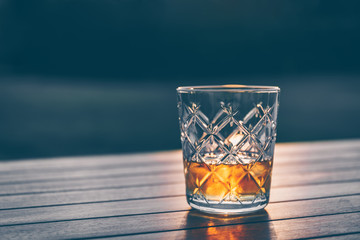 Glass of whiskey on the wooden background during sunset. Relaxation, party, evening out concept