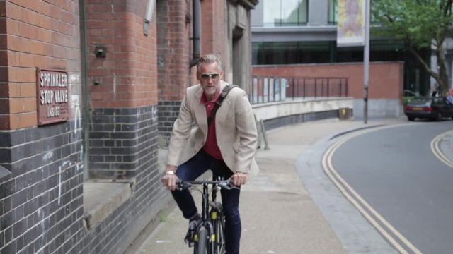 Happy businessman riding bicycle in London, taking phone call