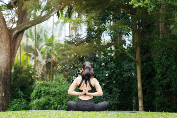 Asian woman practicing yoga in reverse prayer lotus pose, back and shoulders stretching in outdoor park.