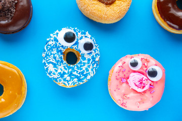 Fototapeta premium A blue donut with a pink donut with funny faces on a blue background looking each other