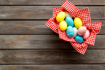 Basket with painted eggs for Easter dinner on dark wooden desk top-down copy space