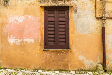 Fototapeta na wymiar Italy, Sicily, Trapani Province, Erice. A wooden shuttered window in on a cobblestone street in the hill town of Erice.