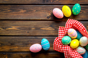 Basket with painted eggs for Easter dinner on dark wooden desk top-down copy space