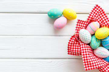 Easter eggs painted in basket on white wooden desk top-down copy space