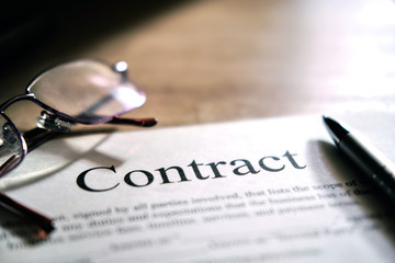 Contract sheet with glasses and a pen on a wooden background