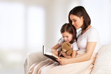 Happy young mother and daughter hugging and reading book