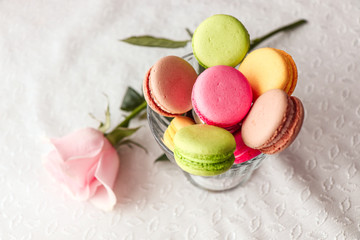 Sweet pink raspberry macaroons on white wooden table with roses on a background. Sweetness concept