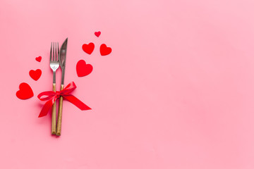 Valentines' Day dating in restaurant concept. Fork and knife decorated with hearts on pink background top-down copy space