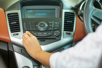 Asian Women press button on car radio for listening to music.