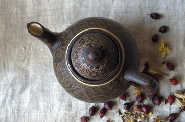 Black oriental tea pot,  dried rose hips and marigold flowers on wooden table coverd with linen canva. Rosehip herbs and marigold aromatic healthy tea in ceramic pot.