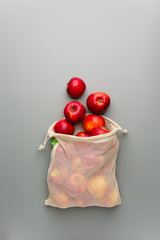 Red apples in a reusable cotton bag on a gray background.