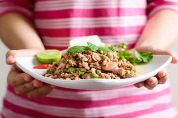 Thai food, spicy minced pork salad (Larb Moo) on white dish holding by hand	