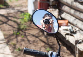 a photographer with a camera is displayed in the mirror of the scooter
