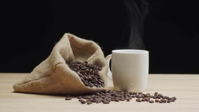 Steamy cup of coffee standing on table near dag with beans, gourmet