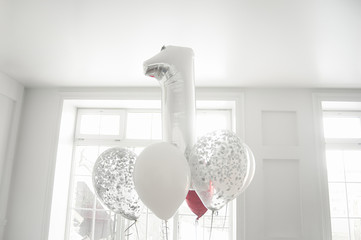 a bunch of white and silver balloons and a foil big silver number one in a white room