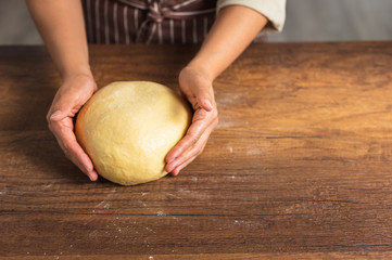 Pair of hands holding a light yellow bread dough on wood surface table top.	