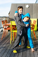 Two boys in their brand new jumpsuits playfully fight on a roof terrace with green and terracotta outdoor furniture