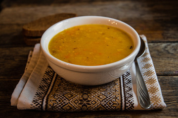 Pea soup in a white ceramic bowl on a kitchen napkin against the background of old wooden boards. Cooking homemade food.