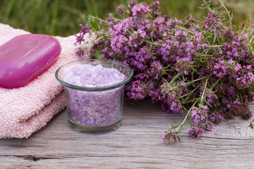 Towel with thyme flowers, bowl with sea salt and soap on wooden background.