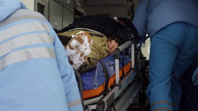 Slowmo tracking of paramedics in uniform loading unconscious patient lying on stretcher into ambulance