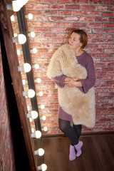 Strange ugly aged woman in in a fur Cape in front of a lighted mirror in a dark room. Old model...