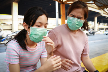 Tired asian child girl with hygienic mask sitting at bus stop,feel sick,woman wearing face mask protection,dirty air prevent PM2.5,air pollution,allergy to dust,bad smell from cars in city Bangkok.