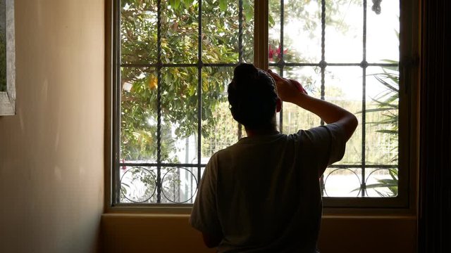 Silhouette of young Latin woman while cleaning window glass at home