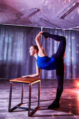 Flexible beautiful gymnast girl doing gymnastic exercises with chair in the hall or on the stage. Young woman jumping in sport dress. Performance and posing actress or dancing model