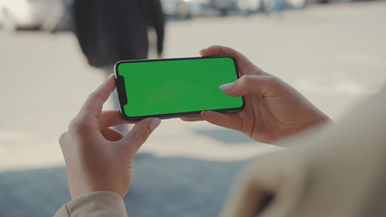 NEW YORK - May 19, 2019: Close up hands woman holding use phone horizontal green screen sitting on street scrolling pages swiping surfing internet technology smartphone message mobile phone slow