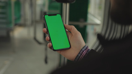 NEW YORK - May 19, 2019: Young man young hand uses holding a mobile telephone with a vertical green screen background tram seat people window key smartphone technology touch message display close up