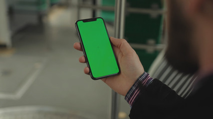 NEW YORK - May 19, 2019: Young man young hand uses holding a mobile telephone with a vertical green screen background tram seat people window key smartphone technology touch message display close up