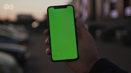 NEW YORK - April 19, 2019: Man holding use smartphone with vertical green screen on night city light background car communication device hands digital gadget phone touchscreen traffic mobile close up
