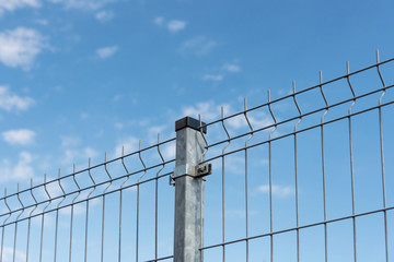 Close-up of a metal fence wire on blue sky background with copy space. 