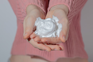 beautiful female hands hold white foam, the girl holds in front of herself full palms of white air cream