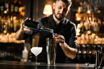 Male bartender pouring an alcoholic drink from the bottle to a steel jigger