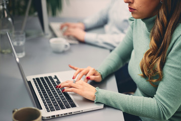 Close up of two coworkers smiling and typing on computer in office.