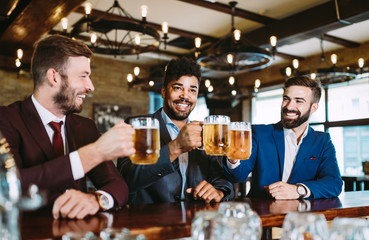 Happy young businessmen drinking beer and talking at pub after work