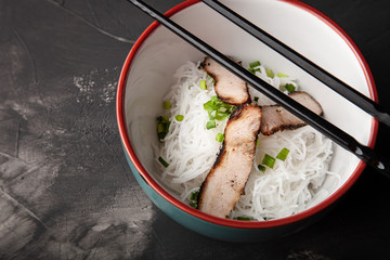 Composition with a bowl of rice noodles, meat and vegetables