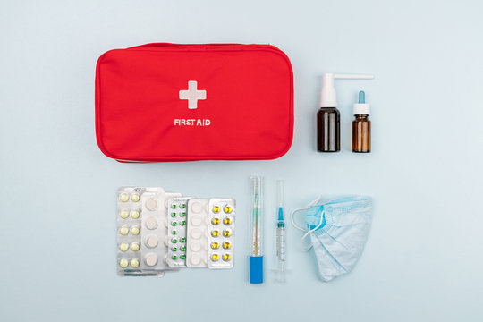 Red home first aid kit. Box for medicines, antibiotics and medicaments. Near pills in a blister packs, thermometer, syringe, mask and throat spray. Flat lay. First aid treatment and healthcare concept