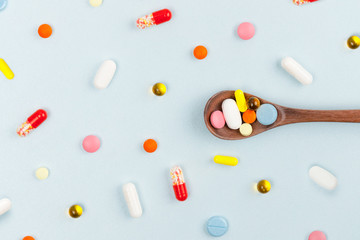 Various colorful multicolored pills on blue background. Tablets in a wooden spoon. Medicines, vitamins, antibiotics and medicaments. Flat lay. First aid treatment and healthcare concept. Pattern.