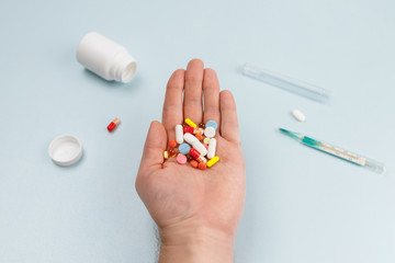 Man hold pile of various colorful pills in hand. Medicines, vitamins and antibiotics. In the background, a jar, a thermometer, and pills. Selective focus. First aid treatment and healthcare concept.