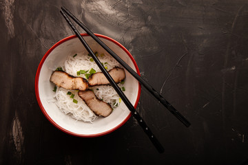 Composition with a bowl of rice noodles, meat and vegetables
