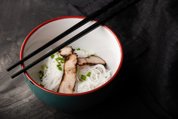 Composition with a bowl of rice noodles, meat and vegetables